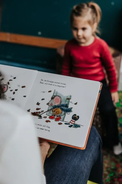 Een kind luistert terwijl een volwassene uit een prentenboek voorleest.